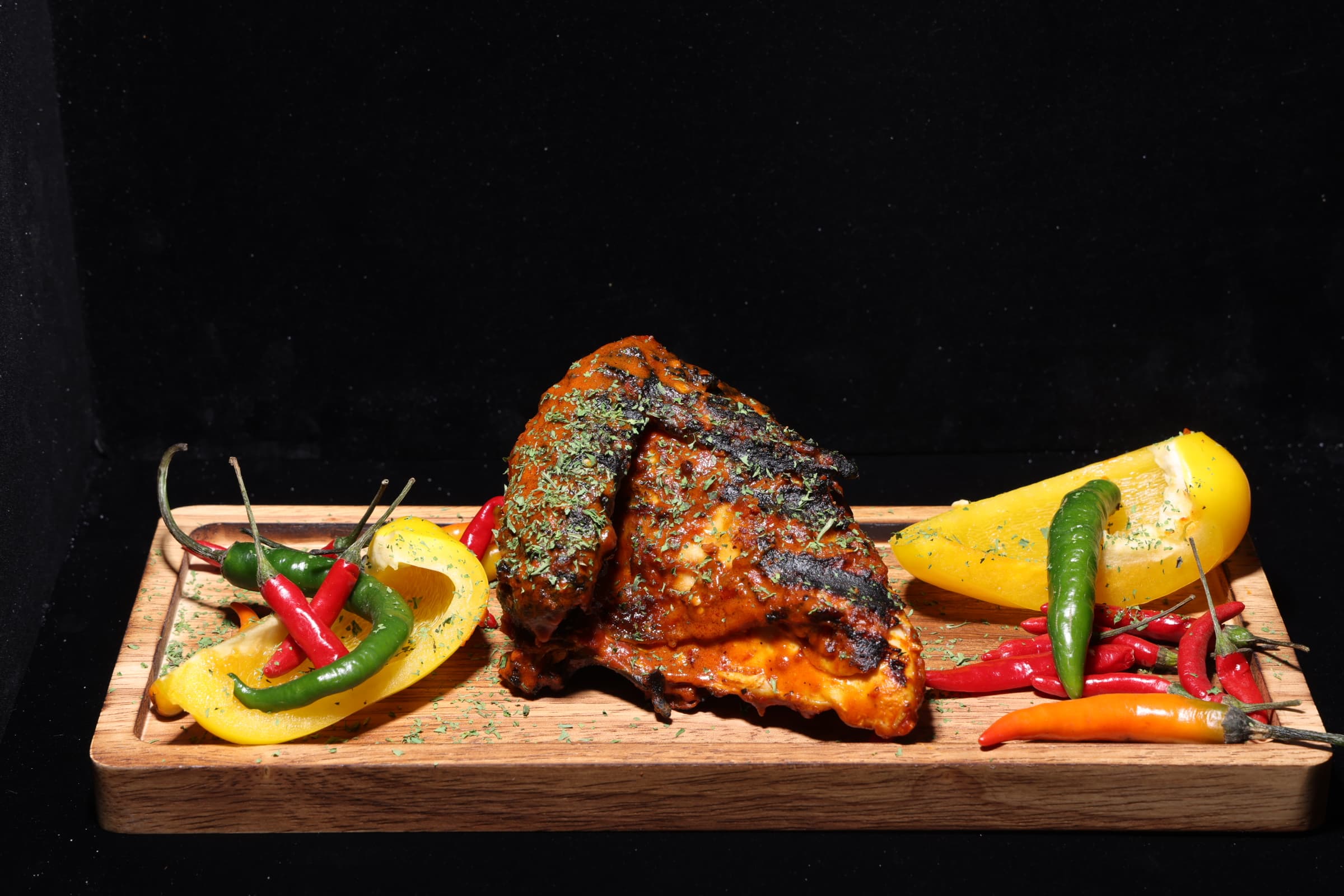 Flame-grilled peri peri chicken with fresh peppers on a wooden board